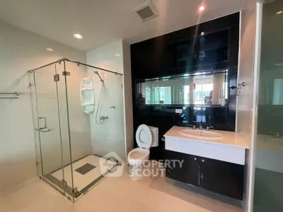 Modern bathroom with glass shower and sleek black vanity in luxury apartment.