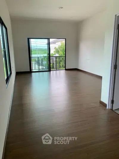 Spacious empty room with wooden flooring and large windows offering natural light.