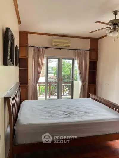 Spacious bedroom with wooden bed frame and balcony view, featuring elegant curtains and ceiling fan.