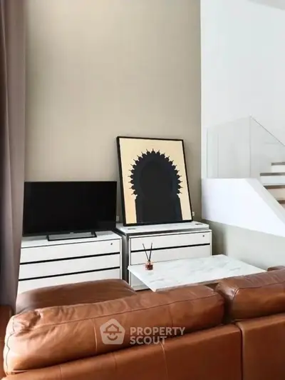 Modern living room with leather sofa, TV, and stylish artwork on a white cabinet.