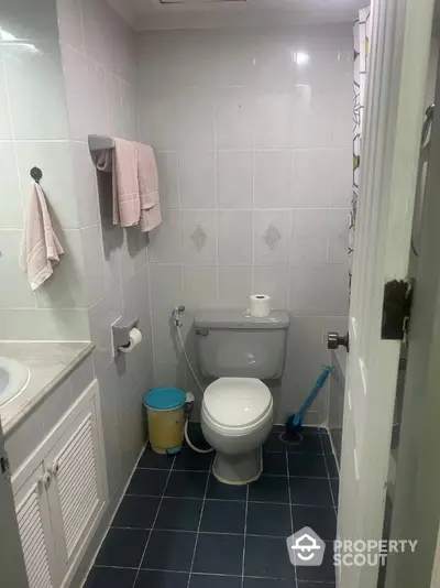 Compact bathroom with tiled walls and floor, featuring a toilet and sink.