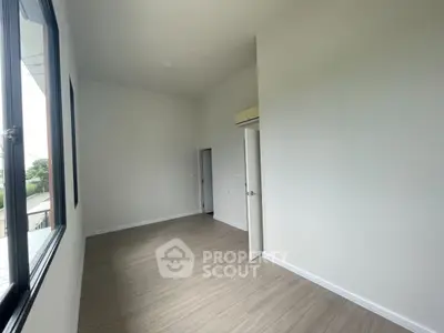 Spacious empty room with large window and wooden flooring, ideal for customization.