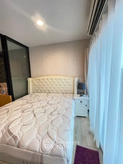 Cozy bedroom with elegant tufted headboard and natural light through sheer curtains.