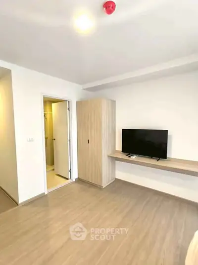 Modern minimalist bedroom with TV and wardrobe, featuring sleek wooden flooring and neutral tones.