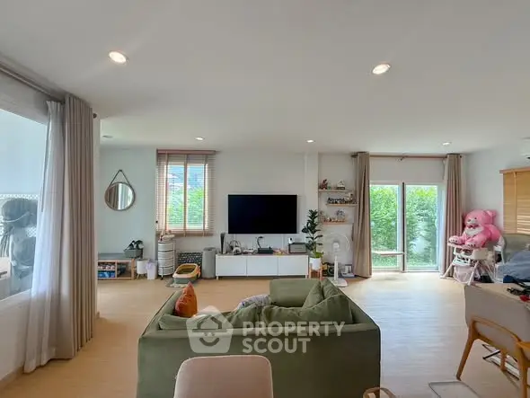 Spacious living room with modern decor and large windows offering natural light and garden view.