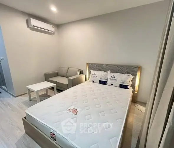 Modern bedroom with minimalist decor, featuring a cozy bed and small sofa, ideal for urban living.