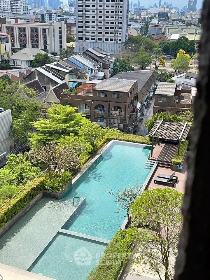 Stunning aerial view of a luxurious residential pool with lush greenery and cityscape backdrop.