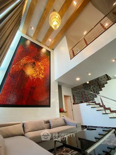 Luxurious modern living room with high ceiling, elegant chandelier, and striking artwork.