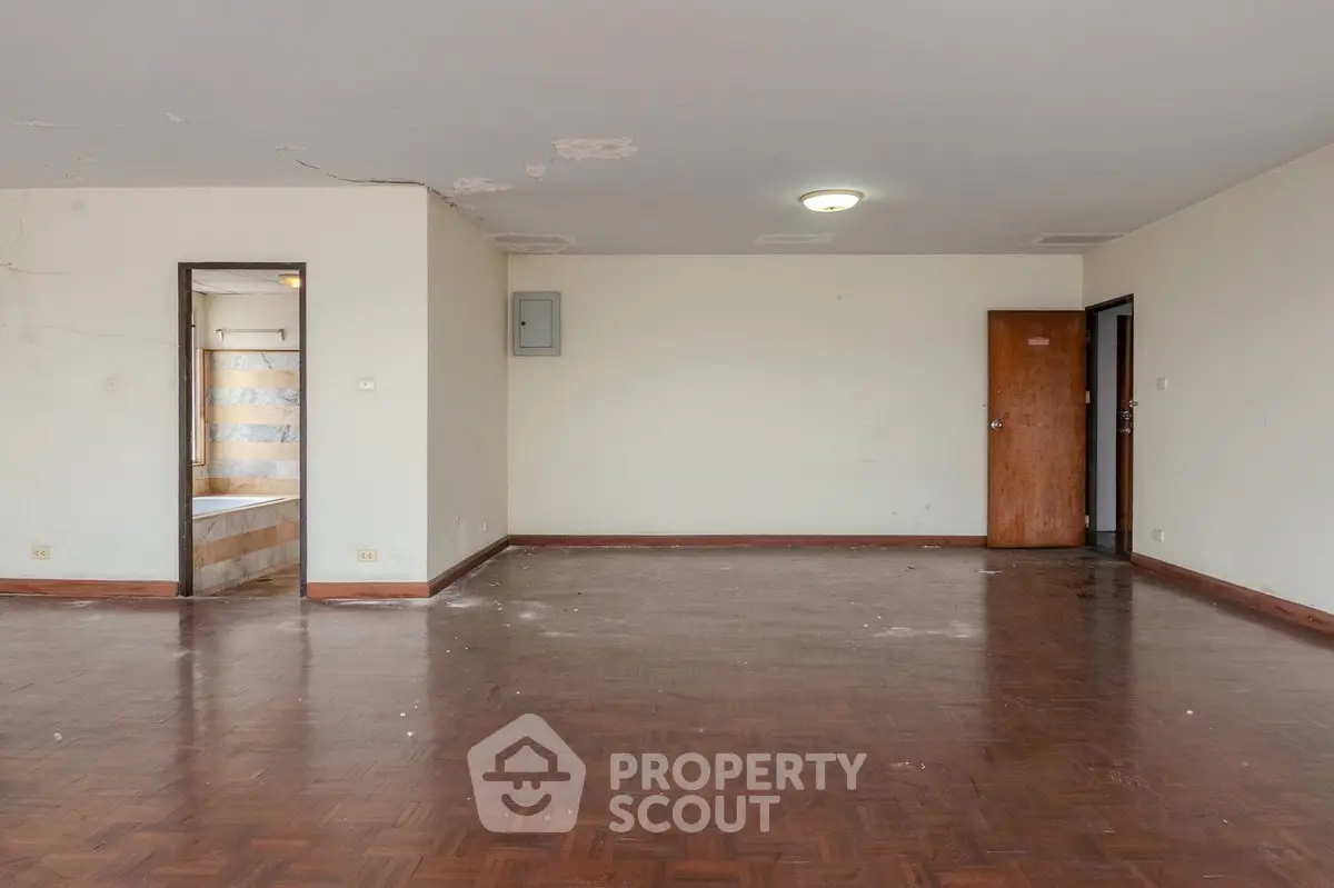 Spacious empty living room with wooden flooring and adjacent bathroom view.