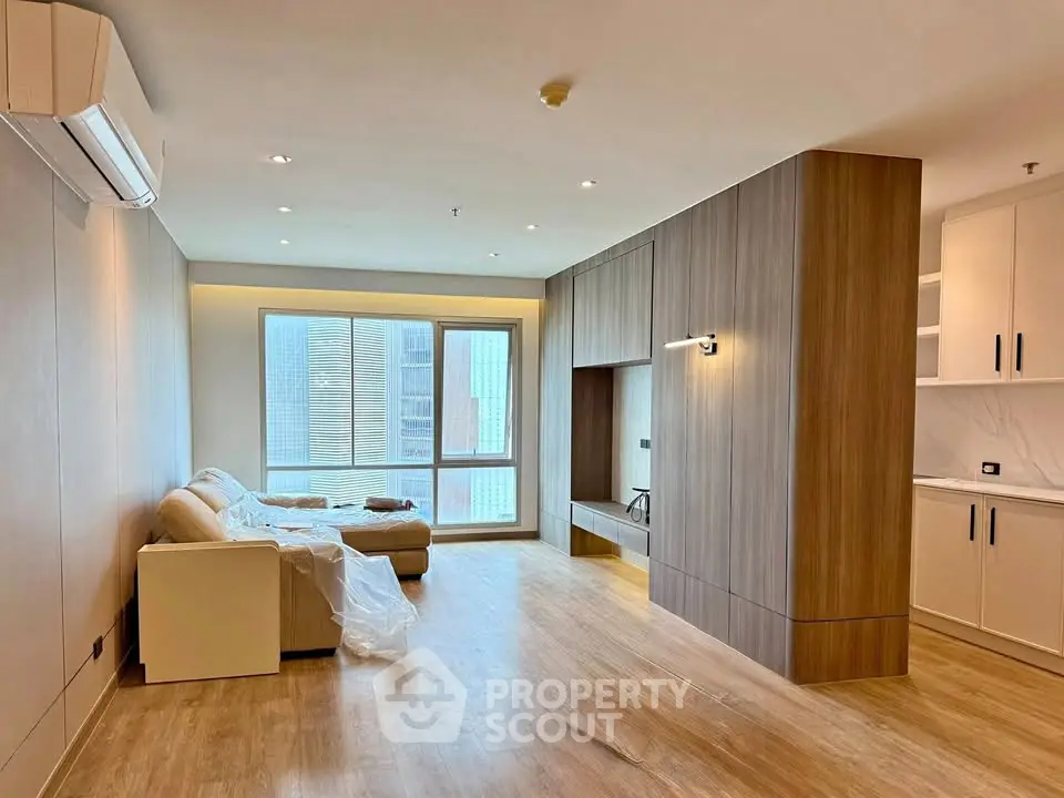 Modern living room with wooden flooring and built-in storage, featuring a cozy sofa and large window.