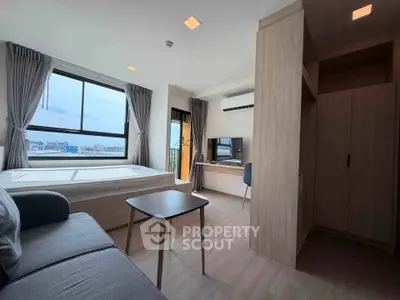 Modern studio apartment with large window and city view, featuring cozy living area and workspace.