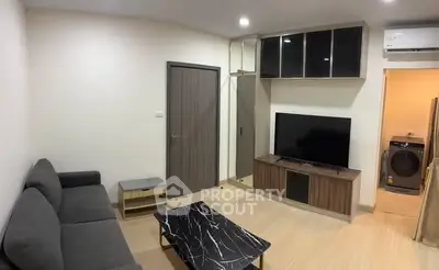 Modern living room with sleek furniture and TV, adjacent to laundry area.