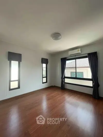 Spacious empty room with wooden flooring and large windows, perfect for customization.
