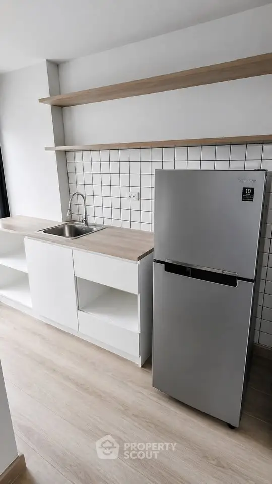 Modern kitchen with sleek fridge and minimalist shelving in a bright apartment.