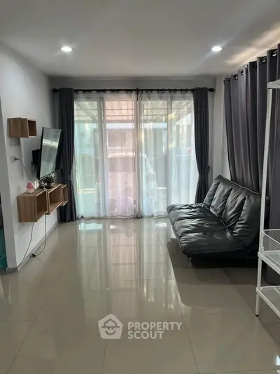 Modern living room with sleek black sofa and large windows offering natural light.