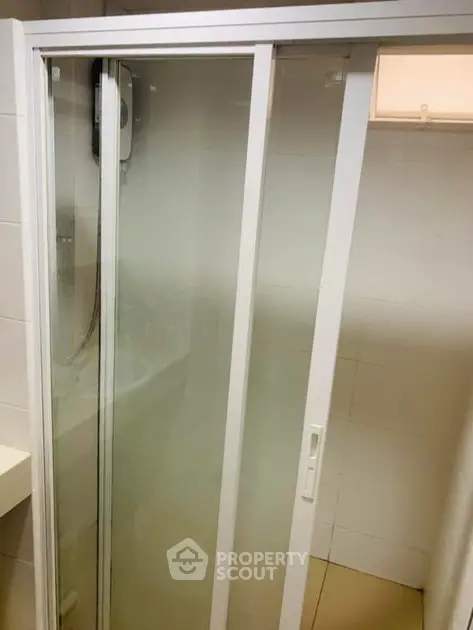 Compact bathroom shower with sliding glass doors in modern apartment.