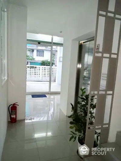 Bright and inviting entrance hall with gleaming tiled floors, modern elevator access, and lush potted plant adding a touch of greenery.