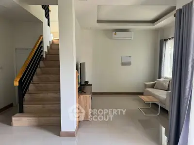 Modern living room with staircase and air conditioning, featuring sleek furniture and natural light.