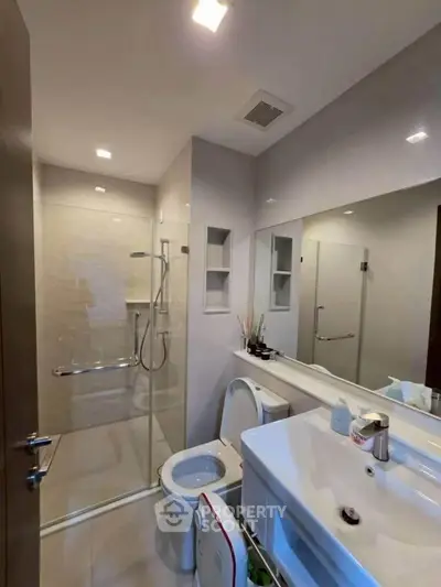 Modern bathroom with glass shower and sleek fixtures in contemporary apartment.
