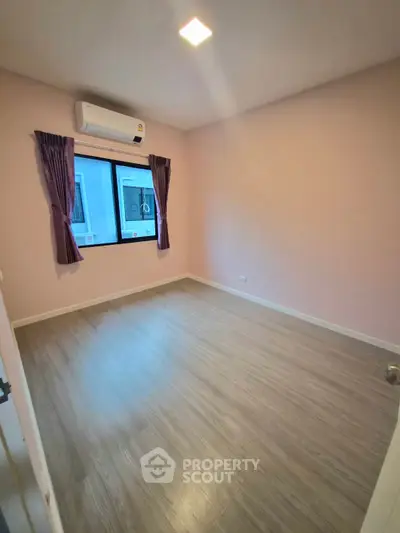 Spacious bedroom with wooden flooring and large window, perfect for natural light.