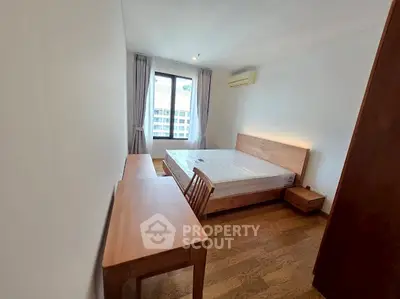 Cozy bedroom with wooden furniture and large window offering natural light.