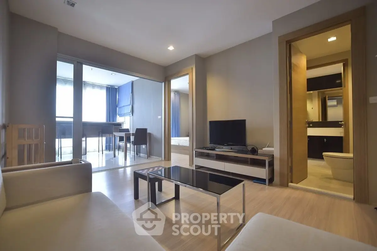Modern living room with open layout and balcony view, featuring sleek furniture and neutral tones.