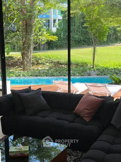 Luxurious living room with pool view and lush garden, featuring elegant black sofa and glass coffee table.