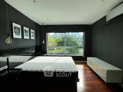 Spacious bedroom with large window offering city and greenery views, featuring modern decor and hardwood floors.