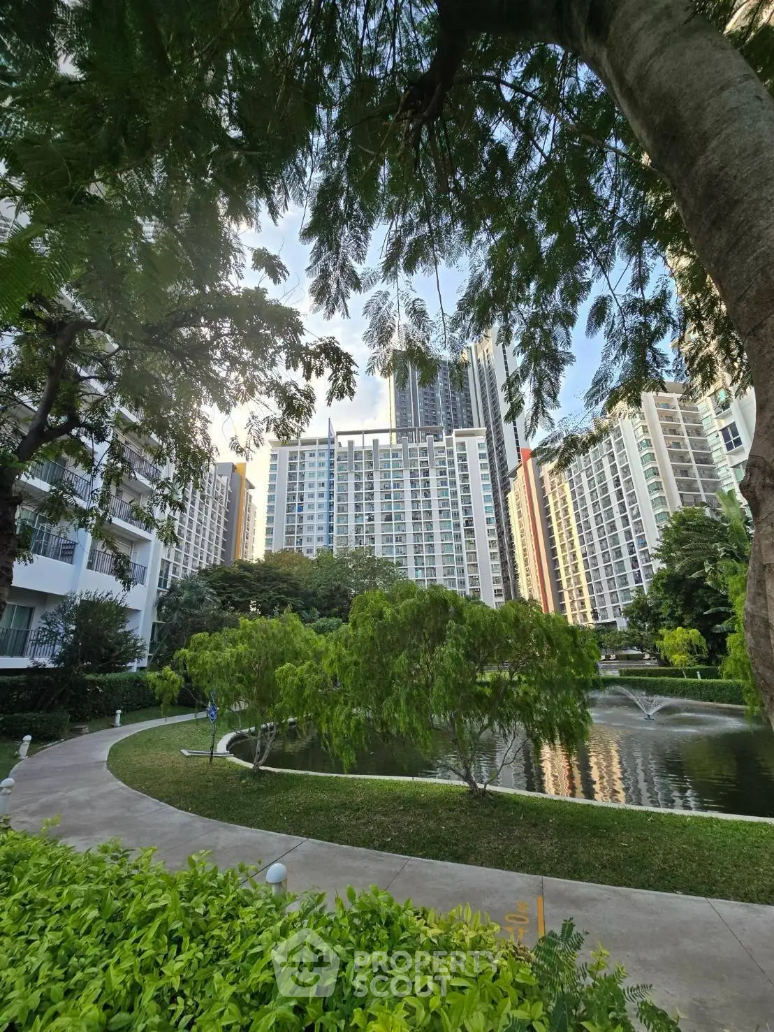 Stunning view of modern high-rise buildings with lush greenery and serene pond in urban setting.
