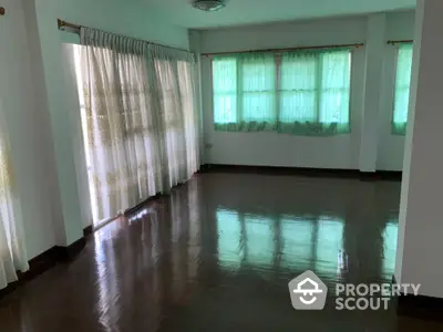 Spacious empty room with polished wooden floors and large windows with curtains