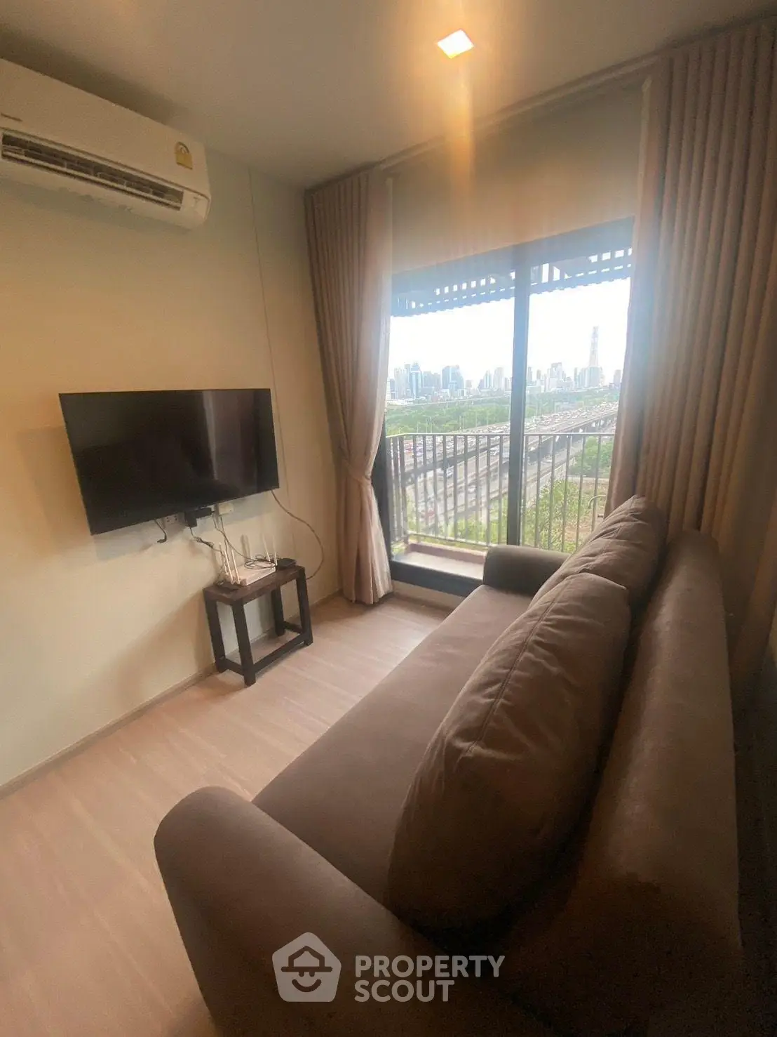 Cozy living room with city view, featuring a comfortable sofa and wall-mounted TV, perfect for relaxation.