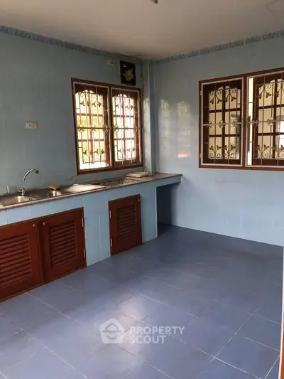 Spacious kitchen with blue tiles and wooden cabinets, featuring natural light from large windows.