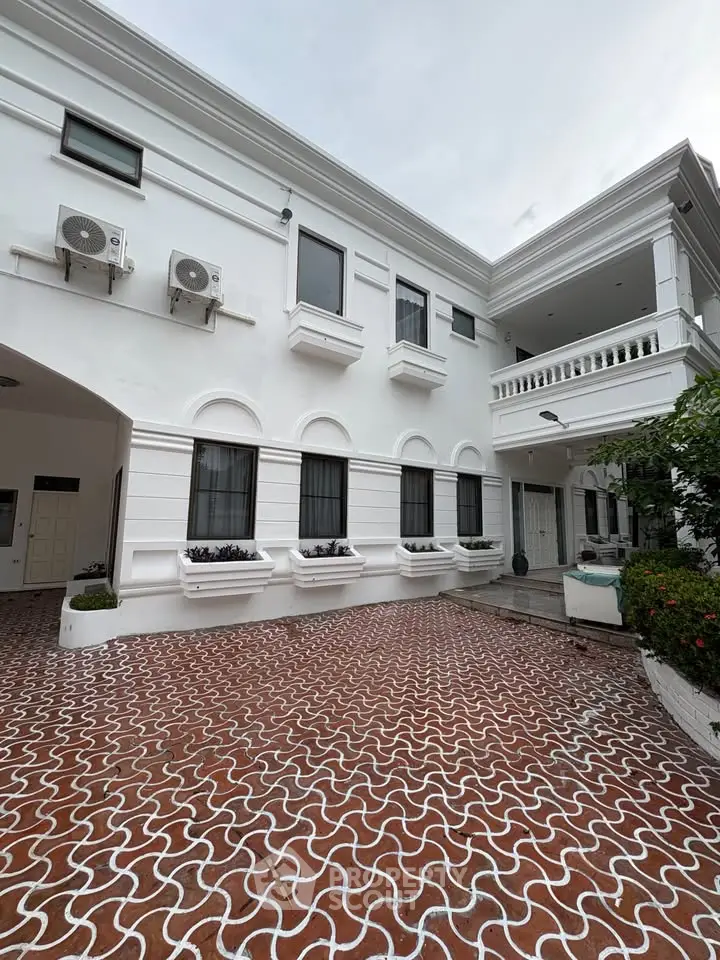 Elegant white building exterior with intricate brick driveway and lush greenery.