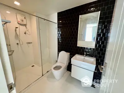 Sleek modern bathroom with glass shower enclosure, black tiled walls, and white fixtures, offering a clean and contemporary look.