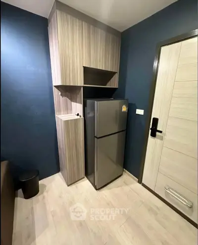 Modern kitchen corner with sleek fridge and stylish cabinetry in compact apartment.