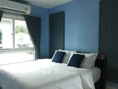 Cozy bedroom with blue walls and large window offering natural light.