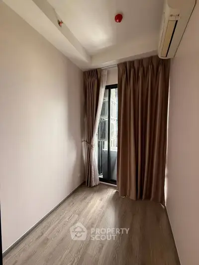 Cozy small room with wooden flooring and large window, perfect for a study or guest room.