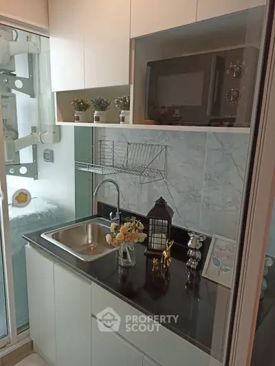 Compact modern kitchen with sleek black countertop and stainless steel sink, featuring decorative accents and microwave.
