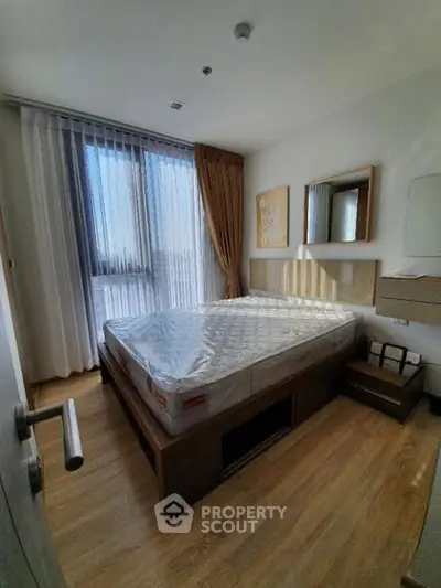 Modern bedroom with large window and wooden flooring, featuring a stylish bed and elegant decor.