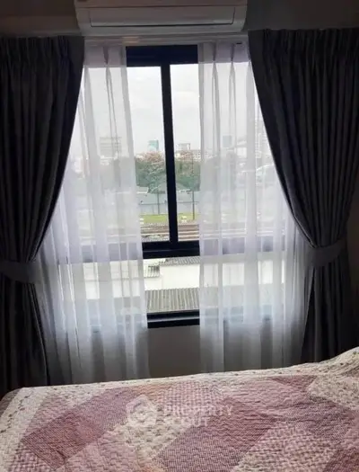 Cozy bedroom with large window offering city view, featuring elegant curtains and a comfortable bed.