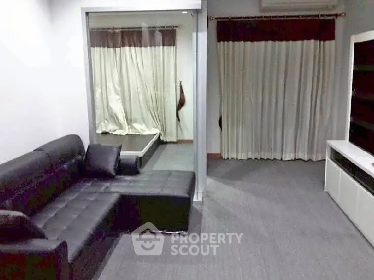 Modern living room with sleek black sofa and large windows with curtains.