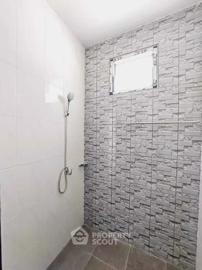 Modern bathroom with tiled walls and showerhead, featuring a small window for natural light.