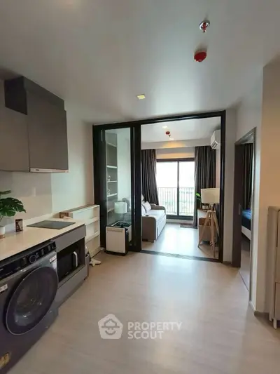 Modern apartment interior with open layout and washing machine, featuring a cozy living area and balcony view.