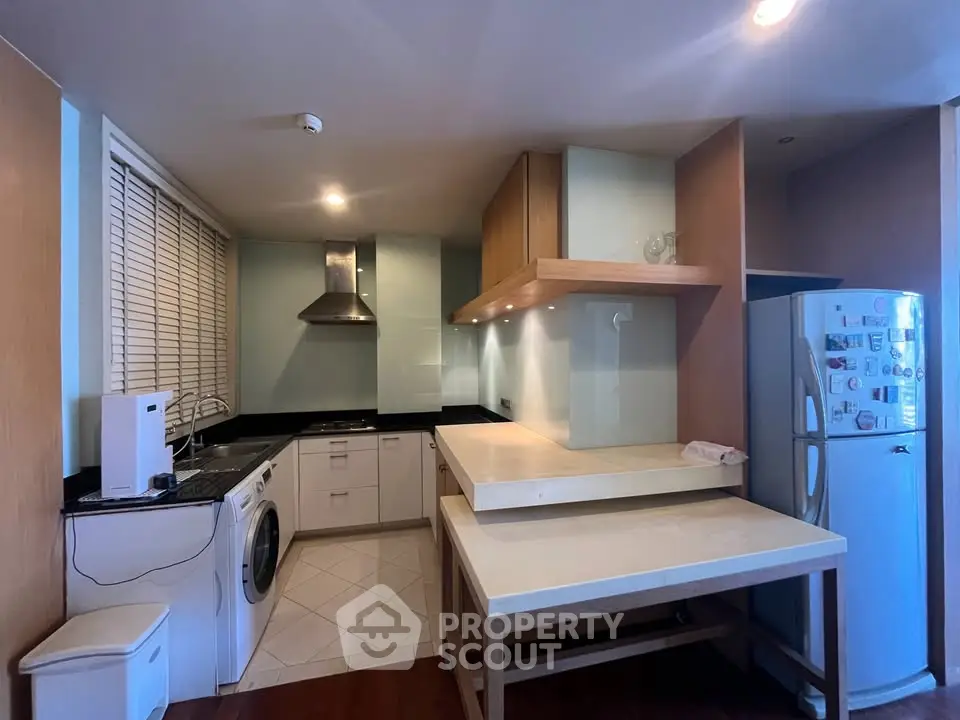 Modern kitchen with sleek appliances and open layout, featuring washing machine and fridge.