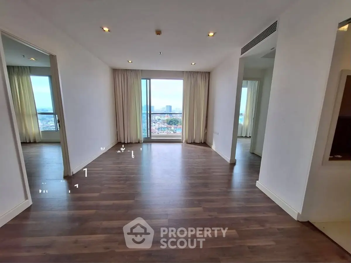 Spacious living room with large window offering stunning city view, featuring elegant wooden flooring and modern lighting.