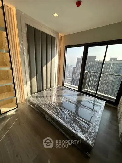 Modern bedroom with floor-to-ceiling windows and city view, featuring a wrapped bed and sleek design.