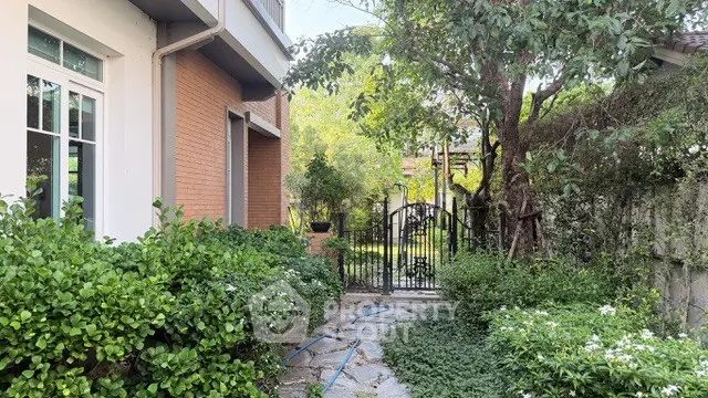 Charming garden pathway leading to a gated entrance with lush greenery and brick exterior.