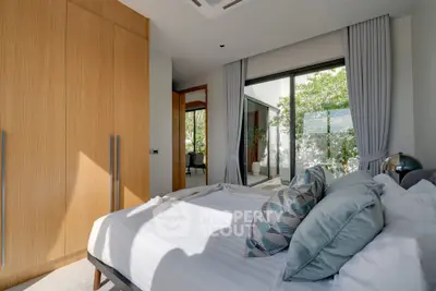 Modern bedroom with large window and stylish decor, featuring wooden wardrobe and cozy bedding.