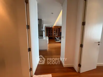 Spacious modern apartment hallway leading to a stylish living area with wooden flooring and built-in shelves.