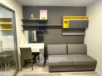 Modern living room with sleek gray sofa, stylish shelving, and compact workspace in a cozy apartment.